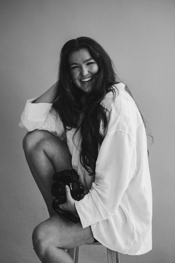 a photo of Maegan Lamm in the studio smiling at the camera, while holding her camera