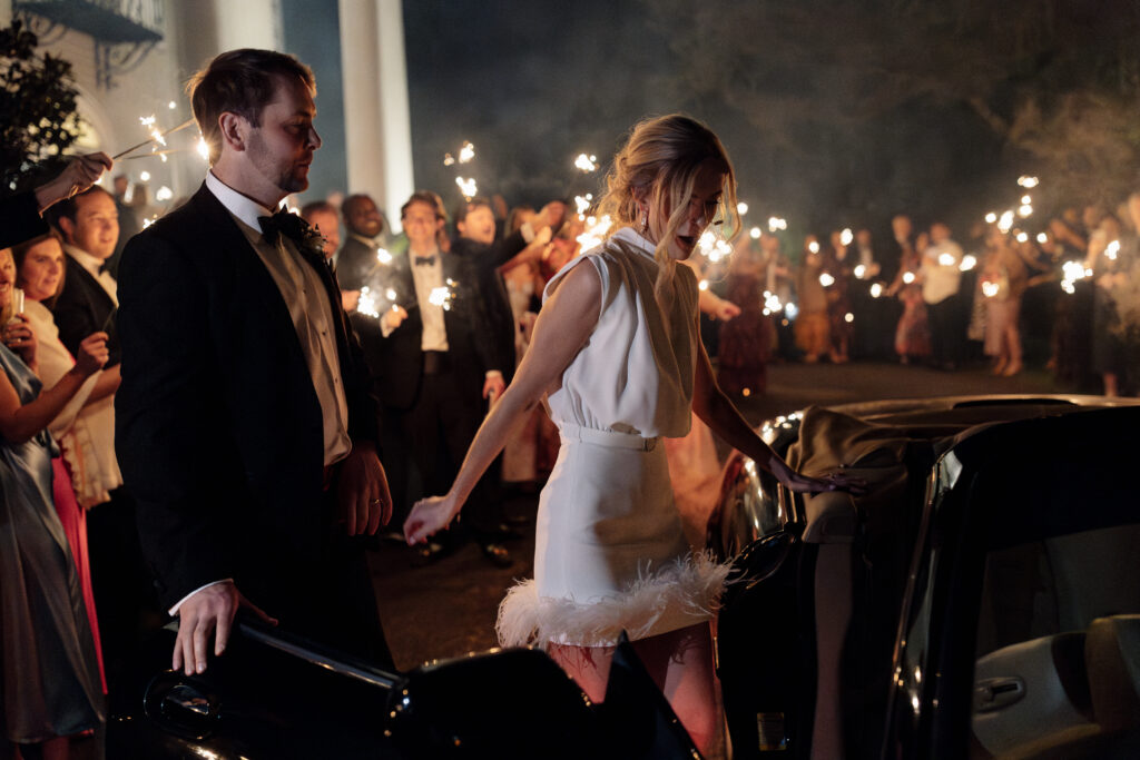 bride getting in getaway car while her groom holds the door for her