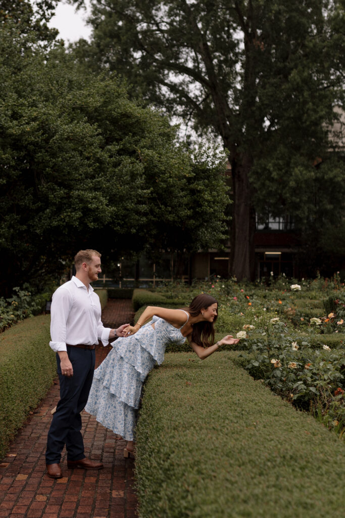 Man holding girl's hand while she leans in to smell the roses