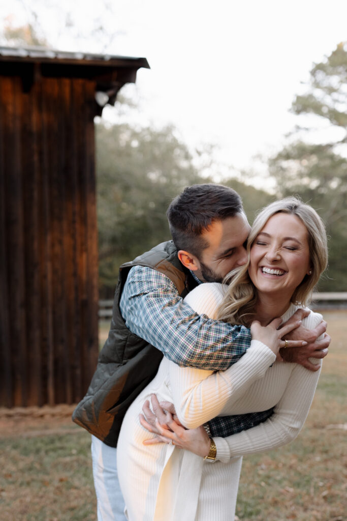 Man hugging his fiance from behind while giving her kisses during their photo session in spartanburg sc