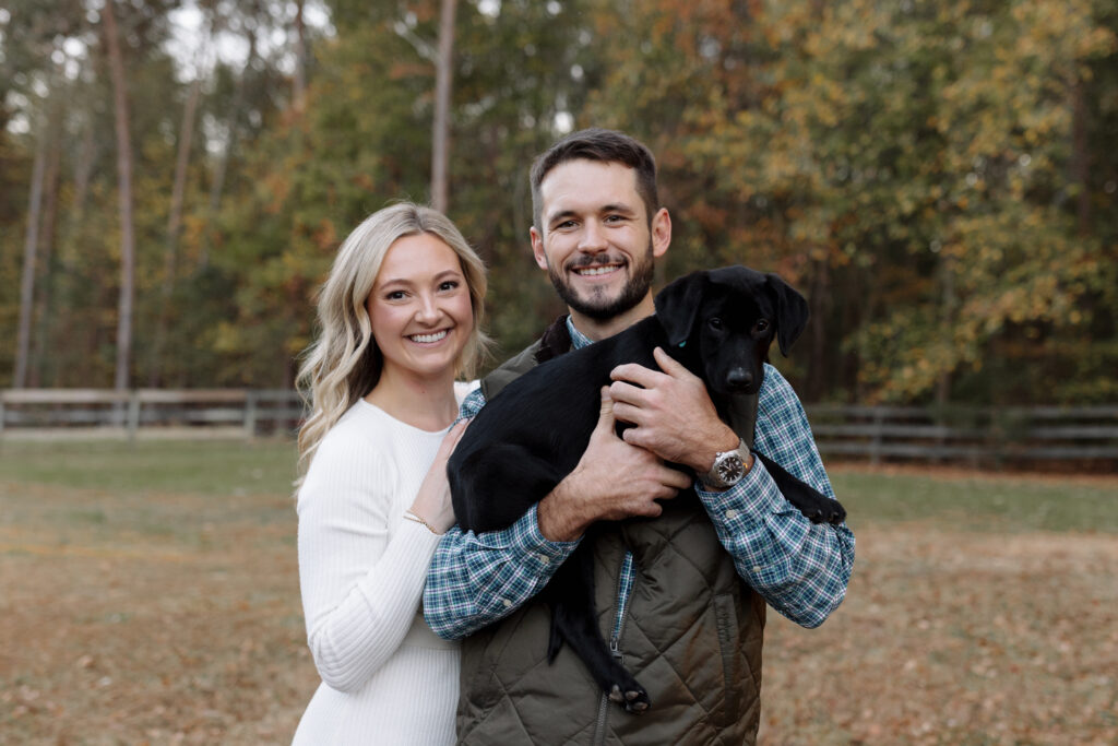 Couple smiling while taking engagement photos with their puppy