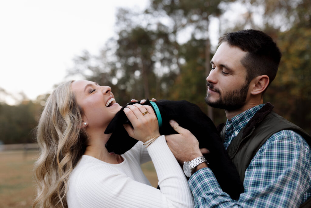 Couple holding their puppy while the puppy licks her face