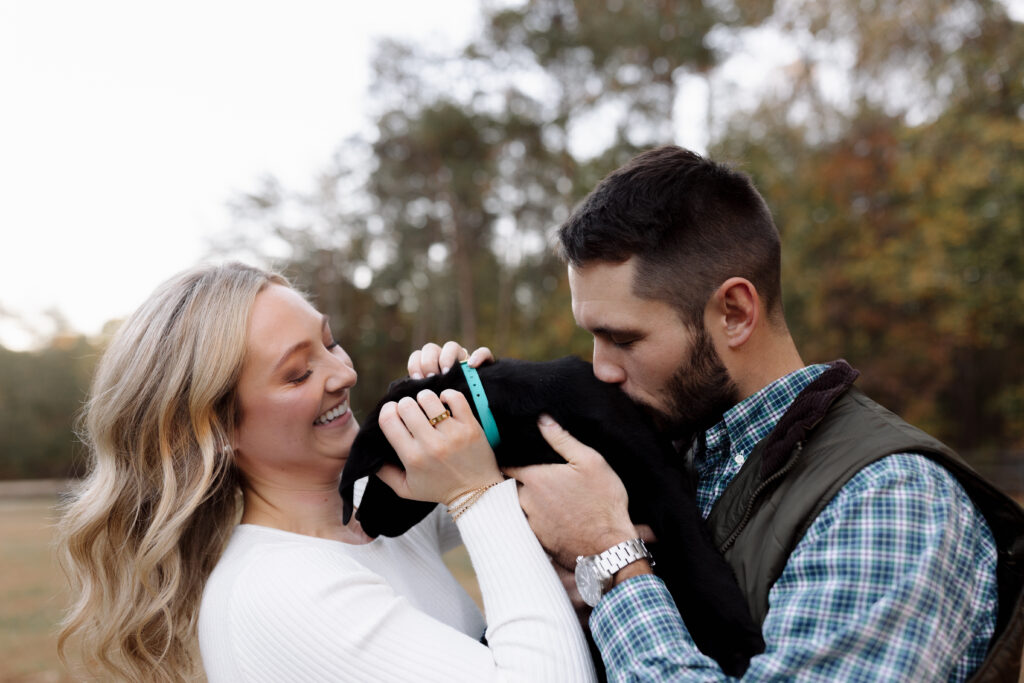 Couple smiling and kissing their puppy