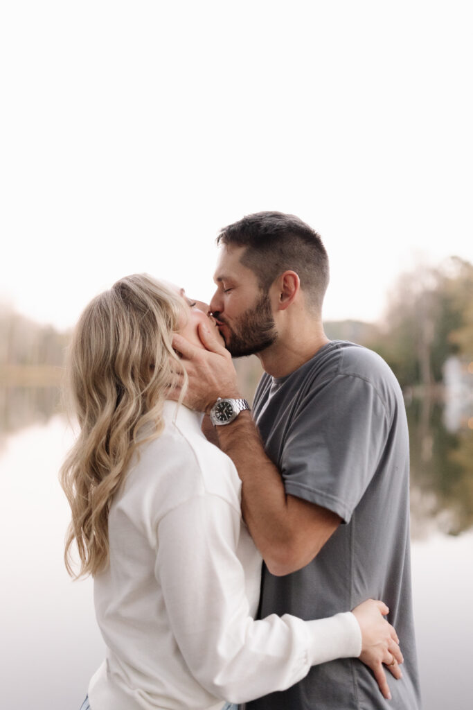 Man holding fiance's face while giving her a kiss by the lake