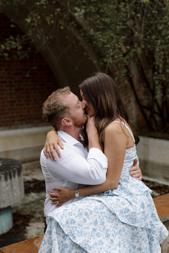 Guy lifting girl's chin to kiss her while she is sitting on his lap