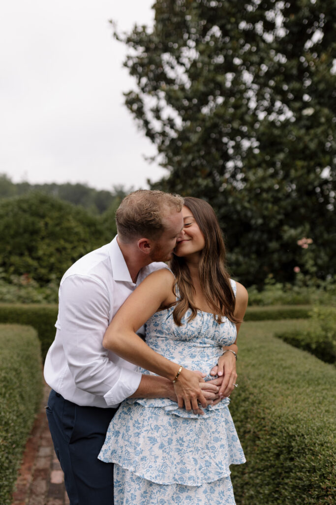 Man hugging fiance from behind and she is leaning into his face smiling