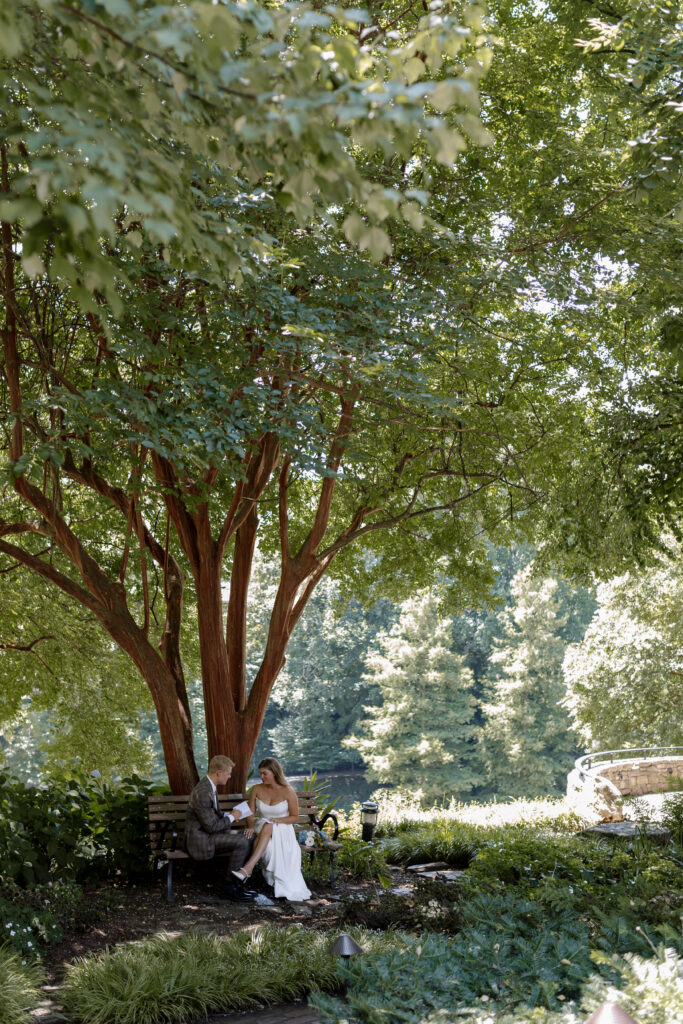 bride and groom in the park on a bench reading their vows