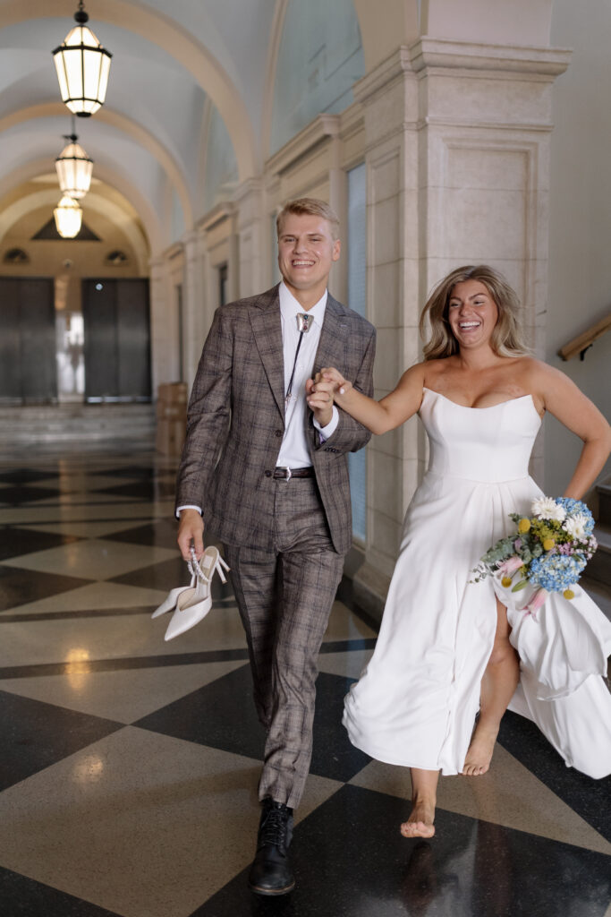 Bride and groom holding hands while running with her bouquet and shoes in hand