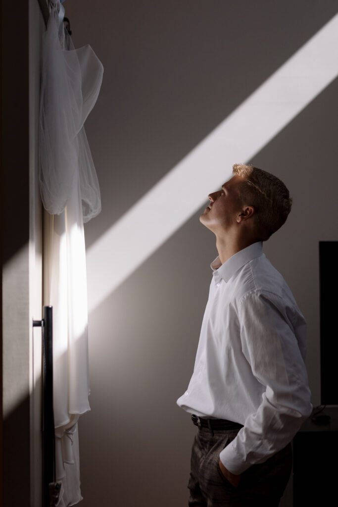 groom looking at the bride's wedding dress hanging above his head