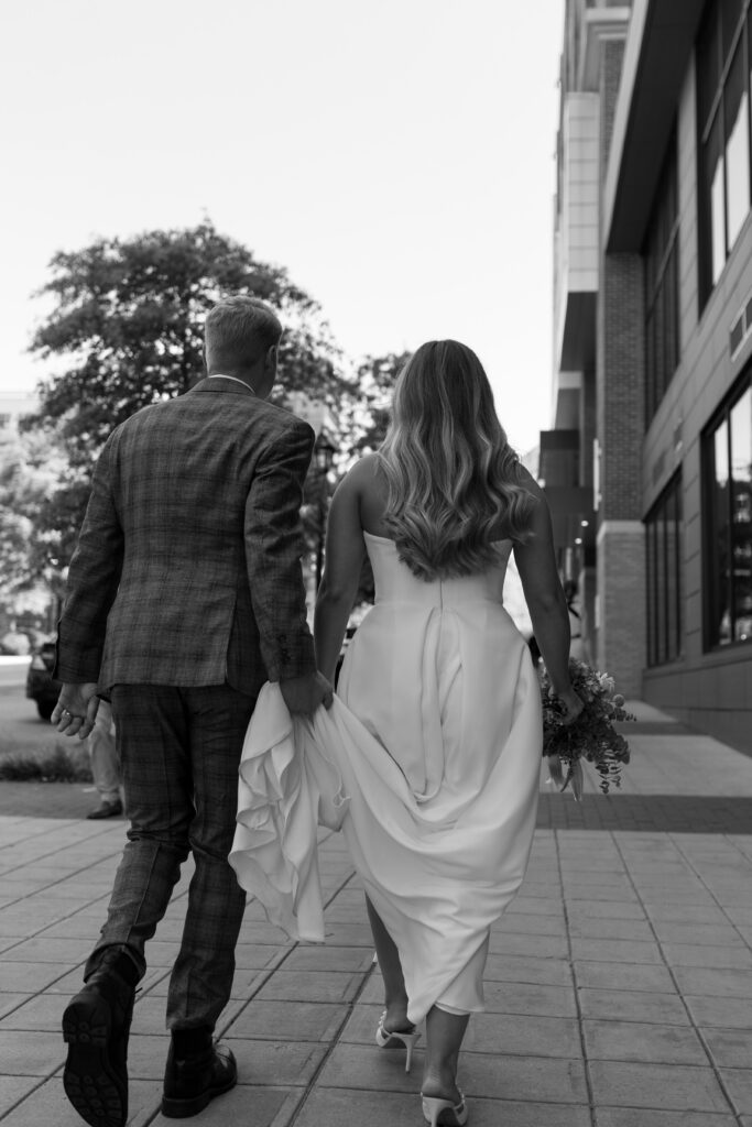 Groom holding bride's train as they walk downtown Greenville sc