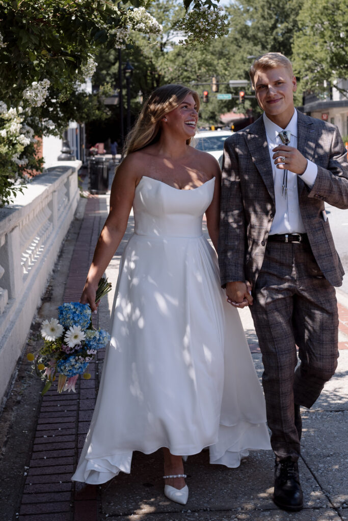 Bride and groom walking on a bridge with flowers over their heads and shadows on their faces