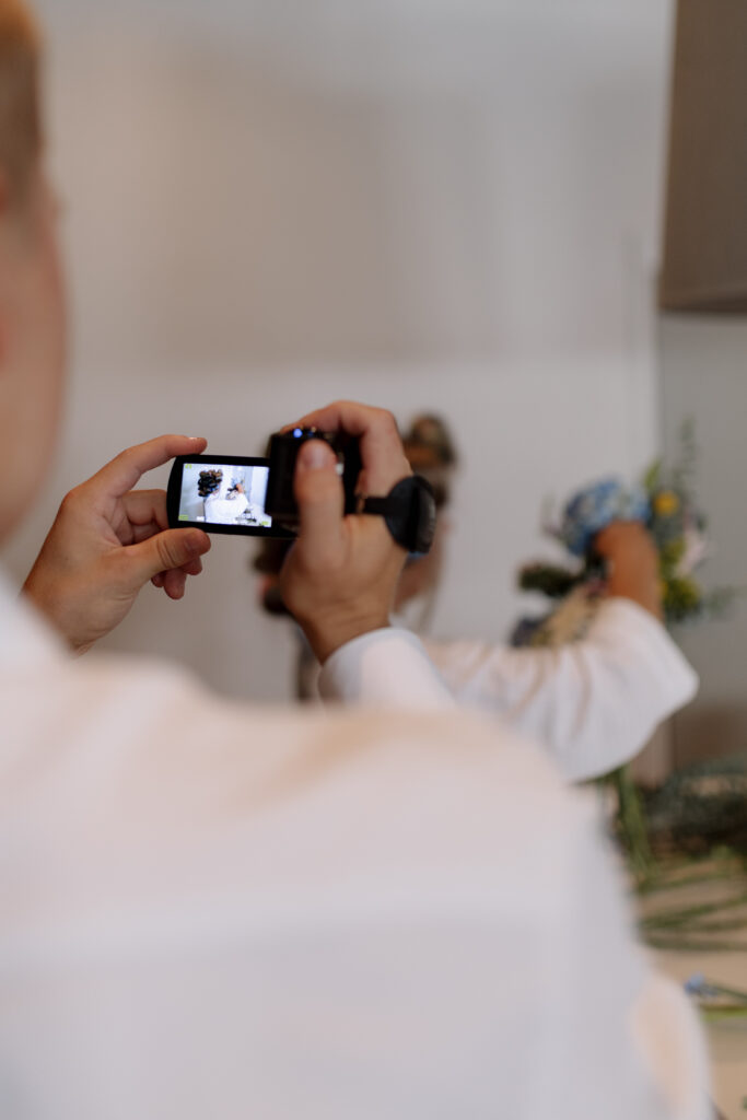 close up of groom video recording his bride putting together her flower bouquet for their wedding