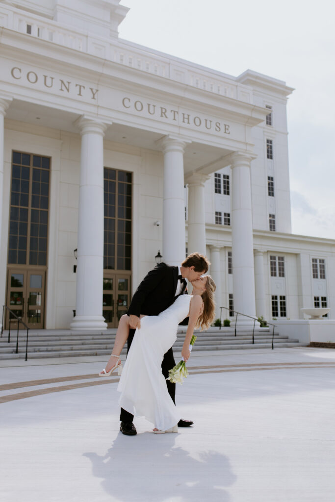 Groom dips bride and kisses her outside the spartanburg county courthouse
