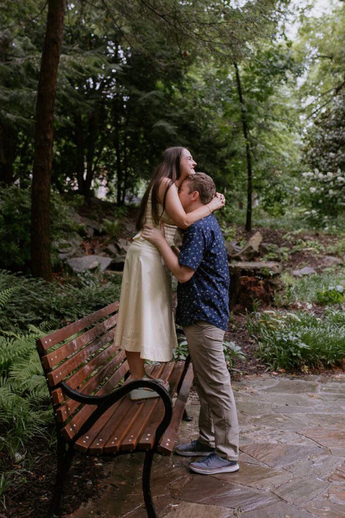 woman standing on bench while man hugs her waist