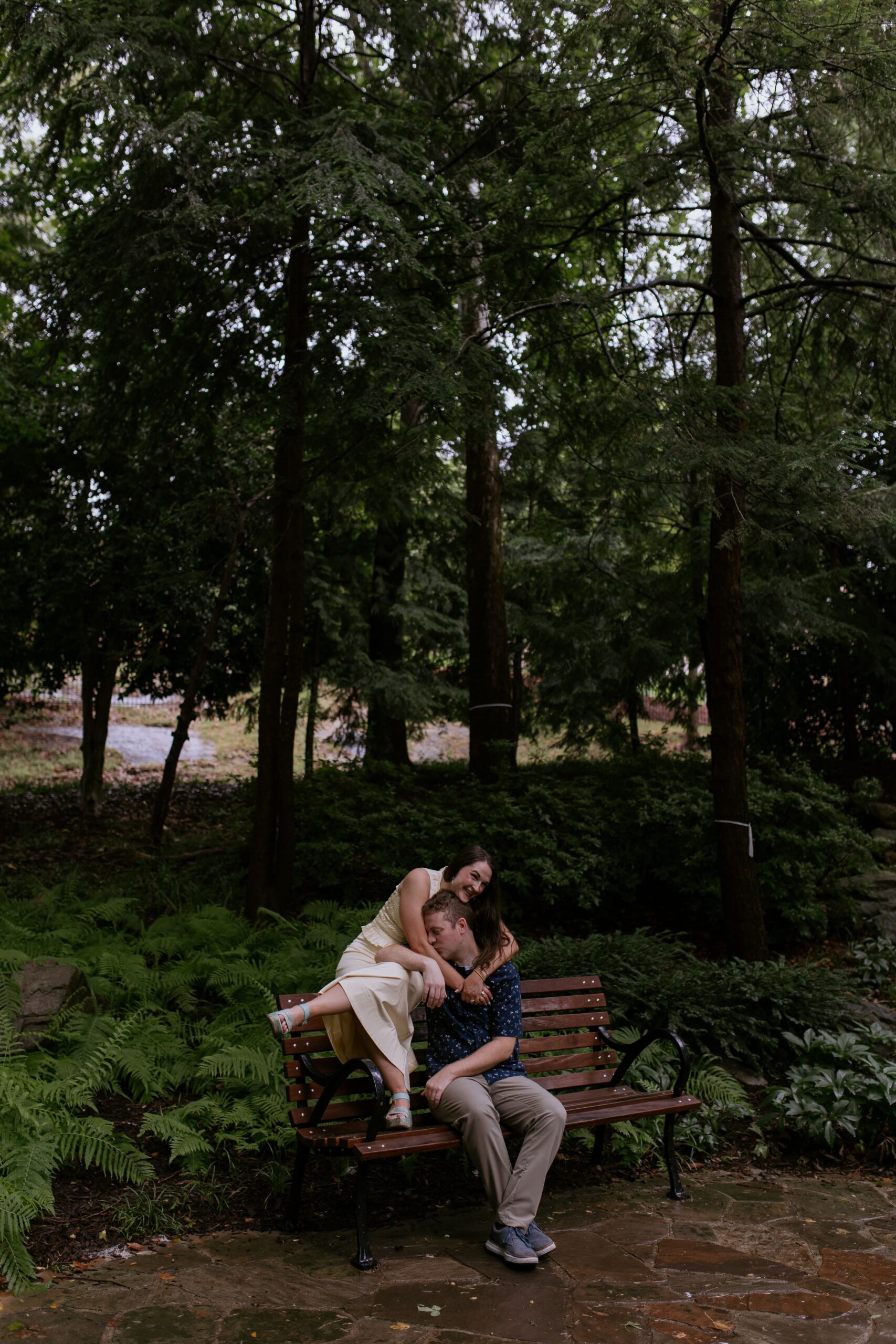 man and woman cuddling while she is sitting on back of a park bench and he is sitting on the bench