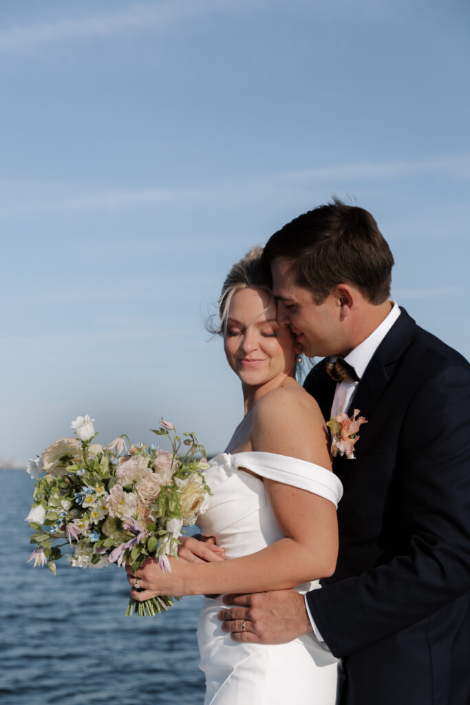 groom hugging bride from behind while she looks down at her flowers